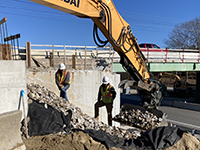 Backhoe drops crushed stone slope at base of abutment 1.